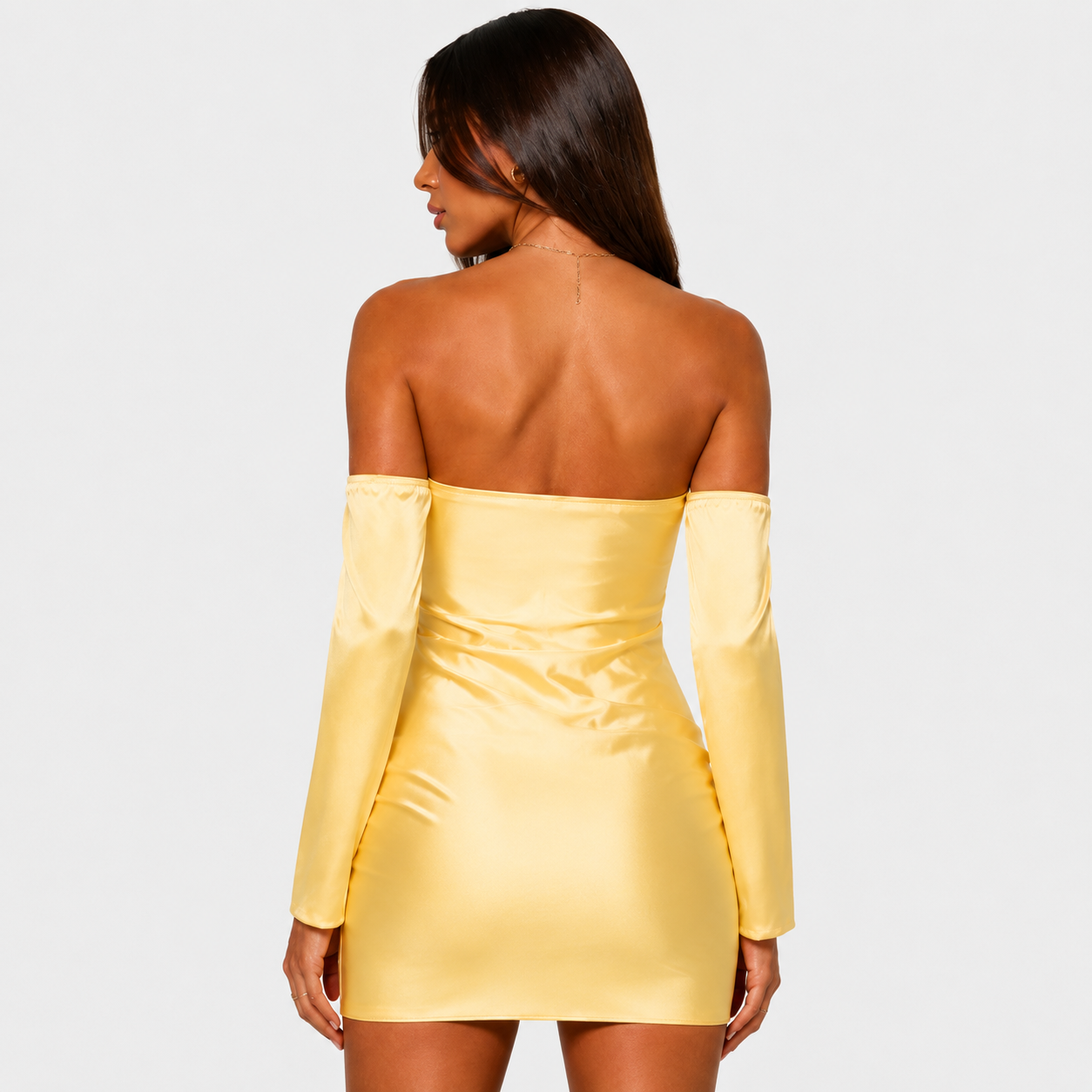 Full-length studio shot of a woman wearing a yellow strapless mini dress with off-the-shoulder long sleeves and black pointed heels, posing against a light gray background.