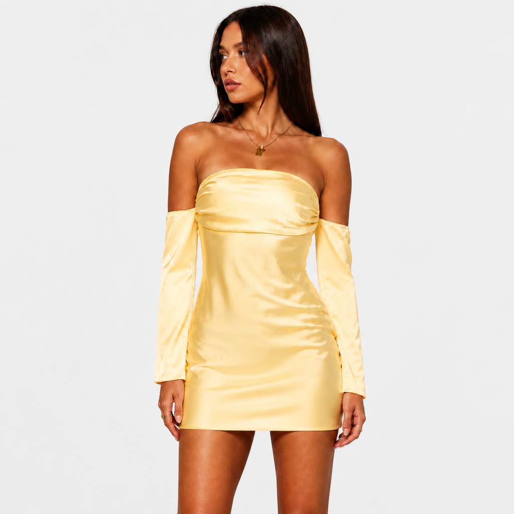 A woman posing in a yellow strapless mini dress with matching detached long sleeves, standing against a light gray background. She has long dark hair and is looking to the side while holding her hair with both hands.