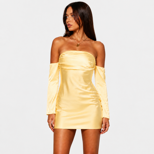A woman posing in a yellow strapless mini dress with matching detached long sleeves, standing against a light gray background. She has long dark hair and is looking to the side while holding her hair with both hands.